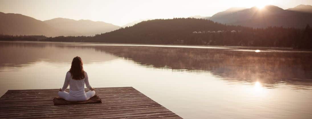 Frau sitzt am Wasser und meditiert / Morgenroutine bei Fibromyalgie